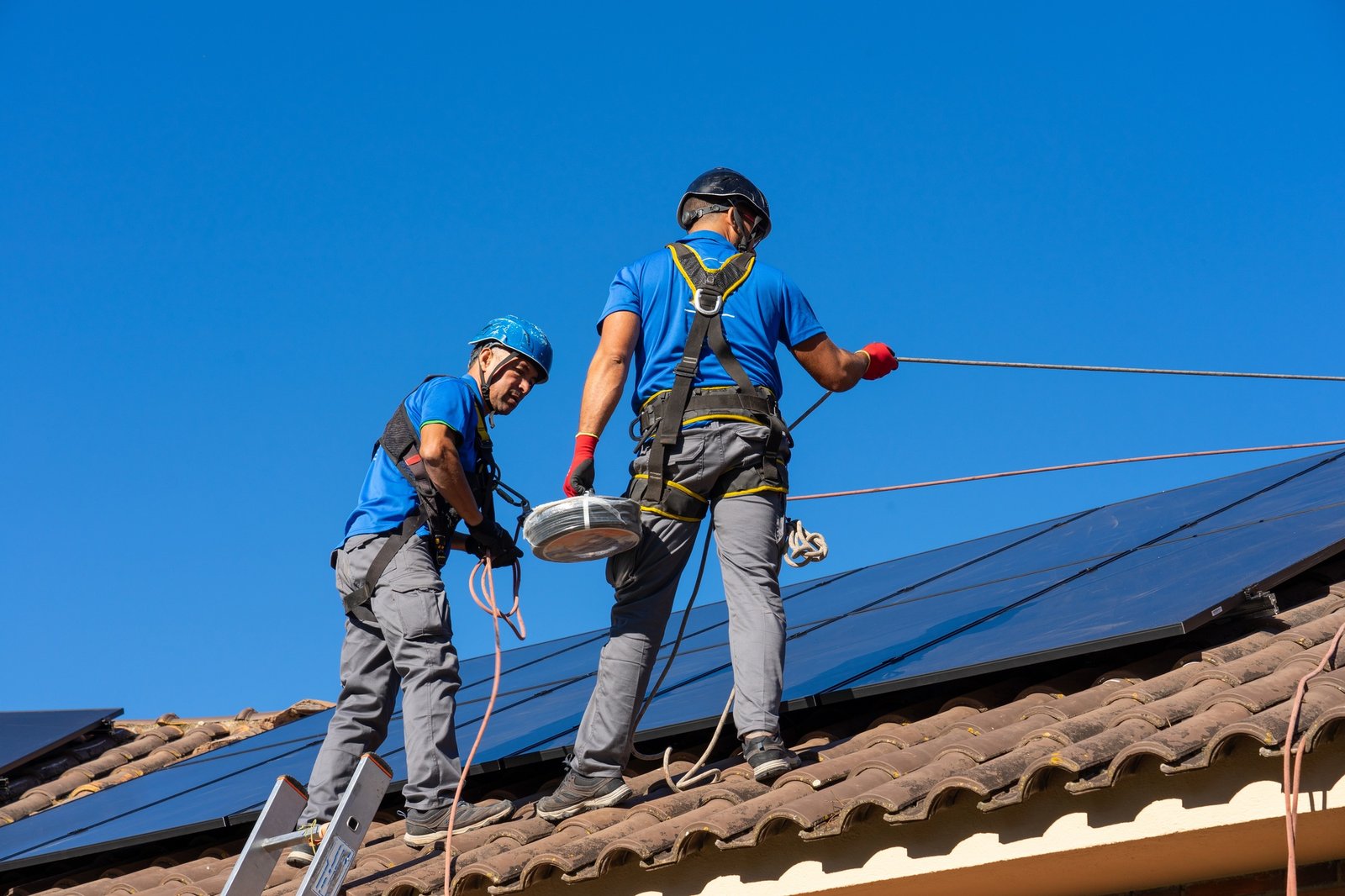 Technicians from AP Sun Energy installing solar panels on a residential rooftop under a bright blue sky, demonstrating professional renewable energy solutions.