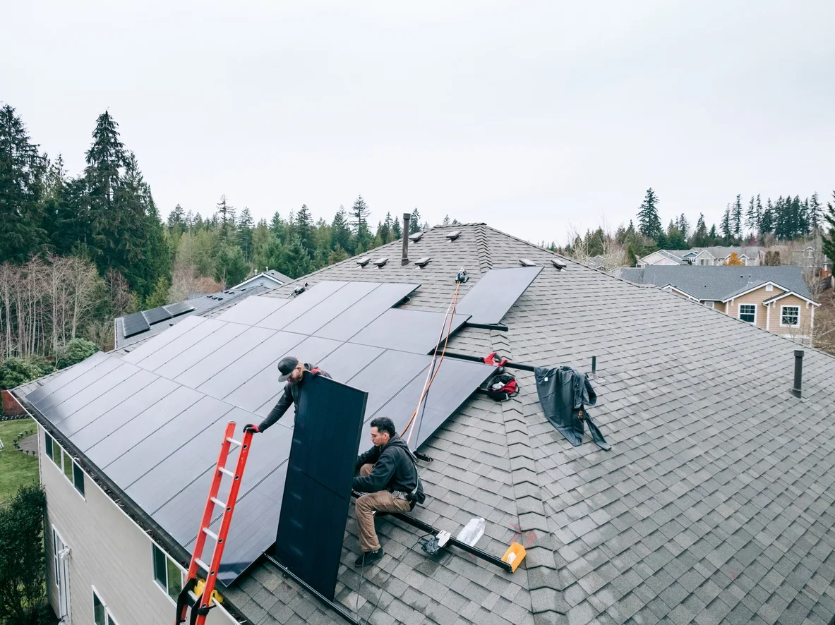 Technicians installing solar panels on a residential rooftop under clear blue skies